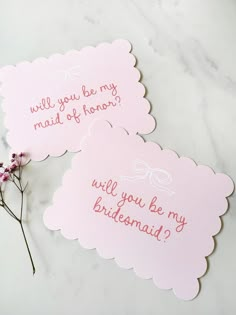 two bridesmaid cards on a marble table with pink flowers in the foreground