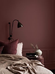 a bedroom with pink walls and bedding in the foreground is a bedside table with a lamp on it