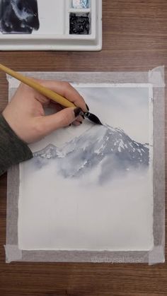 someone is painting a mountain scene with watercolors