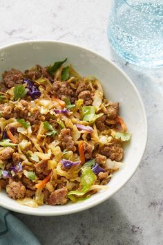 a white bowl filled with meat and vegetables on top of a table next to a glass of water