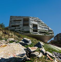 an unusual building on top of a hill with rocks and grass in the foreground