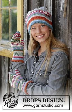 a woman wearing a hat and mittens standing next to a wooden building with an open window