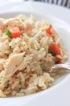 a white plate topped with rice and chicken next to a fork on a tablecloth