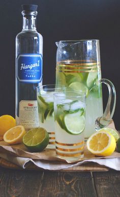 a pitcher and two glasses filled with lemonade, limes, and water on a wooden tray