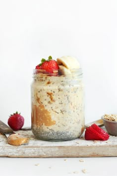 a glass jar filled with oatmeal and strawberries on top of a cutting board