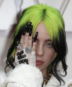 a woman with green hair and black nails holding her hands up to her face in front of the camera