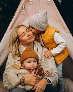 a woman holding a baby in her arms while sitting next to a teepee tent