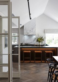 an open kitchen and dining room area with white walls, wood flooring and black bar stools