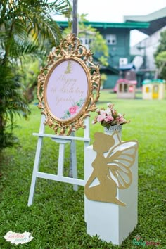 a sign that is sitting in the grass with flowers on it and a butterfly decoration