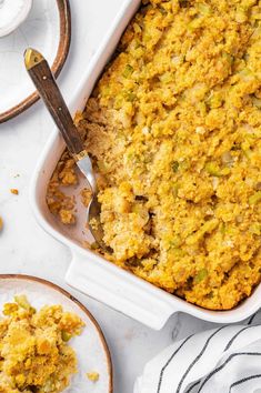 a casserole dish filled with stuffing and topped with a spoon next to two plates