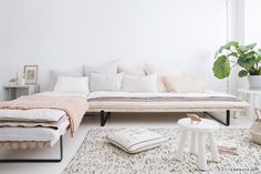 a living room with white furniture and plants in the corner, including a sofa bed