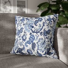 a blue and white pillow sitting on top of a couch next to a potted plant