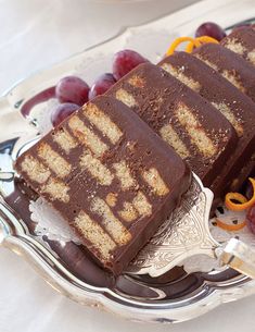 two slices of chocolate cake on a silver plate with grapes and oranges next to it