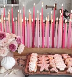 there are many candles that are on the table and in front of some cookies with pink frosting