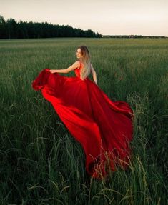 a woman in a red dress is walking through tall grass with her long hair blowing in the wind