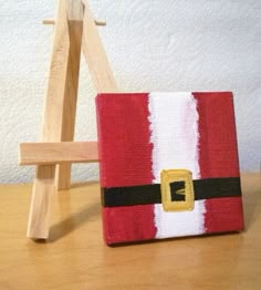 a small wooden easel sitting next to a red and white santa clause christmas bag