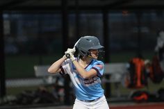 a young woman holding a baseball bat on top of a field