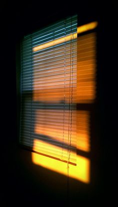 the sun is shining through the blinds in the dark room with it's shadow on the wall