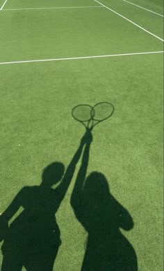 the shadow of a person holding a tennis racket on a tennis court with grass