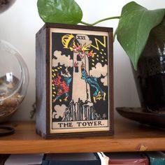 the tower tarot card is sitting on a shelf next to a potted plant