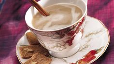 a cup of hot chocolate with cinnamon sticks in it on a saucer next to crackers