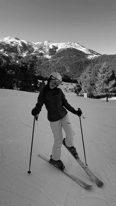 a woman riding skis down the side of a snow covered slope with mountains in the background