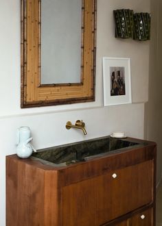 a bathroom sink sitting under a mirror next to a wall mounted faucet in front of a wooden cabinet