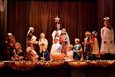 a group of children dressed up in costumes on stage with christmas lights and decorations around them