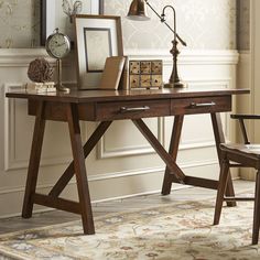 a wooden desk topped with a lamp next to a chair and framed pictures on the wall