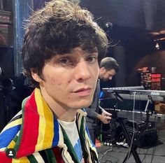 a young man is standing in front of a microphone and recording equipment while wearing a multicolored sweater