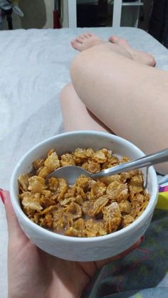 a person holding a bowl of cereal on top of a bed