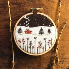 a hand embroidered wall hanging with a red barn and trees in the snow