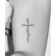 a small cross tattoo on the left side of the thigh, with two leaves attached to it