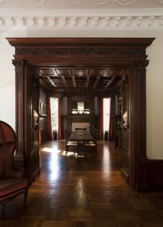 an empty room with wooden floors and carved wood trimming on the walls, along with two red chairs