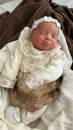 a newborn baby wearing a white bonnet and dress is laying on a brown blanket with her eyes closed