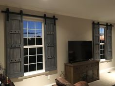 a living room filled with furniture and two windows covered in shutters, next to a flat screen tv