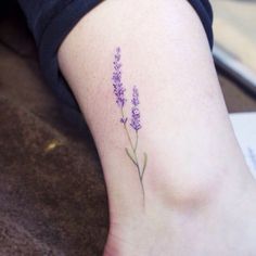 a purple flower tattoo on the left side of the leg, with words below it