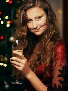 a woman holding a wine glass in front of a christmas tree