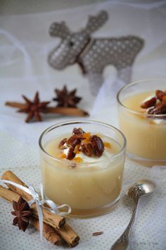 two glasses filled with pudding on top of a white table cloth next to cinnamon sticks