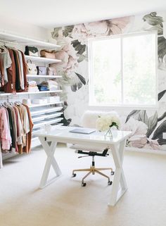 a white desk sitting in front of a window next to a wall with flowers on it