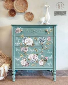 a blue dresser with flowers painted on it and baskets above the drawers, next to a teddy bear