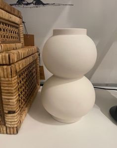 a white vase sitting on top of a table next to a wicker basket and lamp