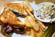 a white plate topped with a cut in half sandwich next to fries and coleslaw