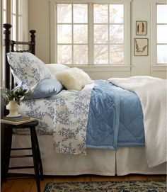 a bed with blue and white comforters in front of a window, next to a rug on the floor