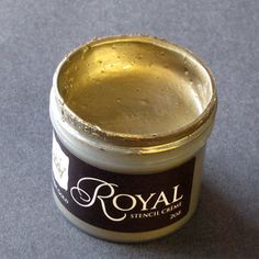 a small jar of gold colored paint sitting on top of a gray surface with the word royal written in it