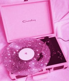 an open pink record player sitting on top of a white bed covered in sparkles