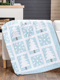 a blue and white quilted christmas tree design on a chair in front of a fireplace