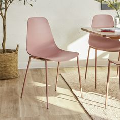 two pink chairs sitting on top of a wooden floor next to a table and potted plant