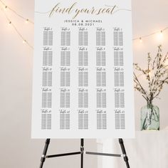 a white table plan on a tripod with string lights in the background and a vase full of flowers