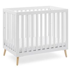 a white crib with wooden legs and a mattress in the bottom half, on a white background